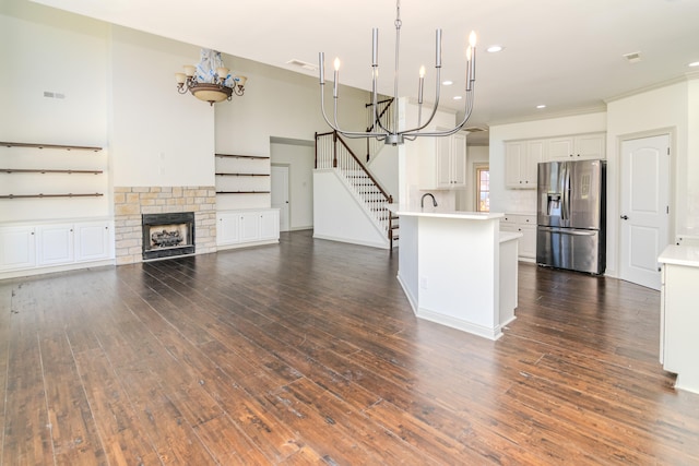 kitchen with stainless steel fridge, white cabinets, dark hardwood / wood-style flooring, a stone fireplace, and a center island