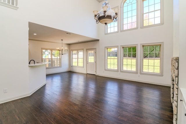 unfurnished living room featuring dark wood-type flooring, crown molding, a towering ceiling, and an inviting chandelier