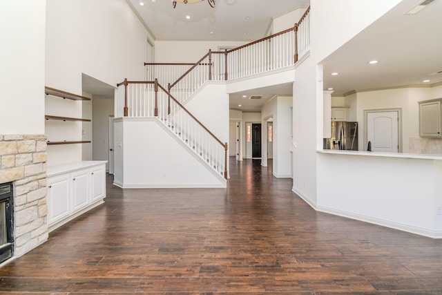 unfurnished living room with a fireplace, a towering ceiling, and dark hardwood / wood-style floors