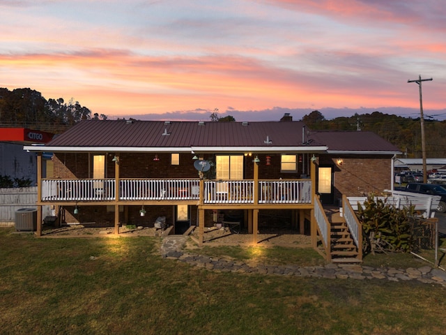 back house at dusk featuring a wooden deck, a yard, and central air condition unit