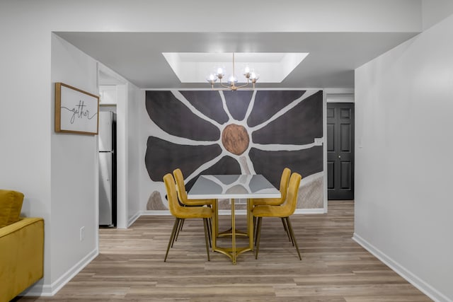 dining space featuring an inviting chandelier, light hardwood / wood-style floors, and a raised ceiling