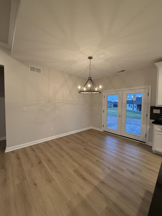 unfurnished dining area with a chandelier, french doors, and light wood-type flooring