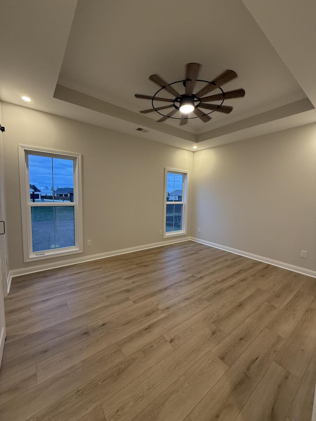 empty room with ceiling fan, light hardwood / wood-style floors, and a raised ceiling