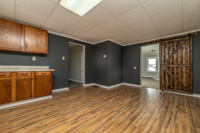 unfurnished living room with ornamental molding, a barn door, a paneled ceiling, and light hardwood / wood-style floors