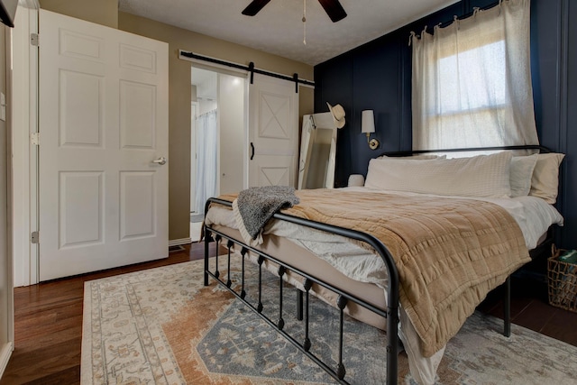 bedroom with dark wood-type flooring, a barn door, and ceiling fan