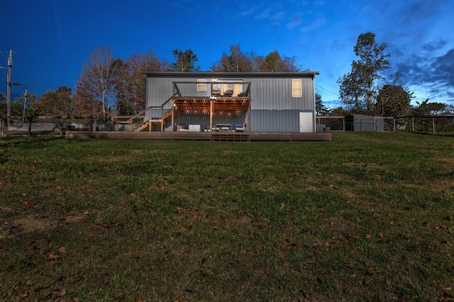 back house at dusk featuring a wooden deck and a yard