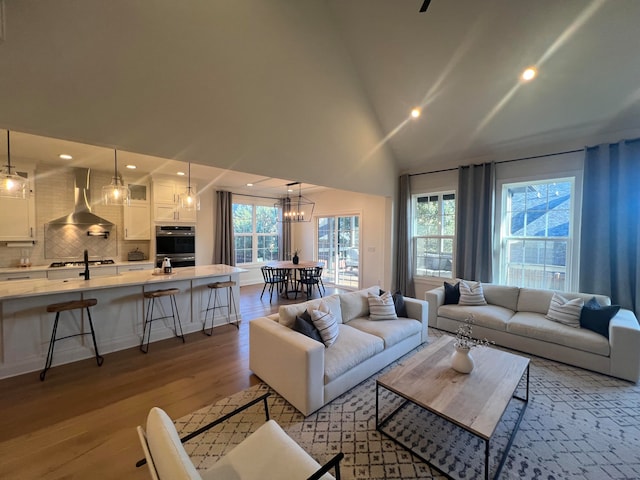 living room with light wood-type flooring, an inviting chandelier, and vaulted ceiling