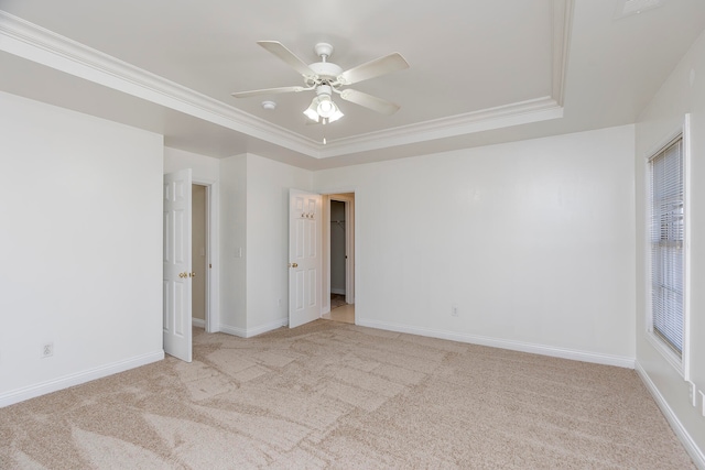 unfurnished bedroom featuring ceiling fan, a raised ceiling, crown molding, and light colored carpet