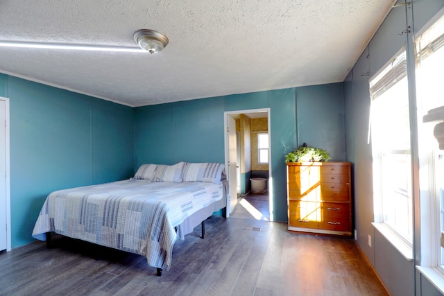 bedroom with a textured ceiling, connected bathroom, multiple windows, and dark wood-type flooring