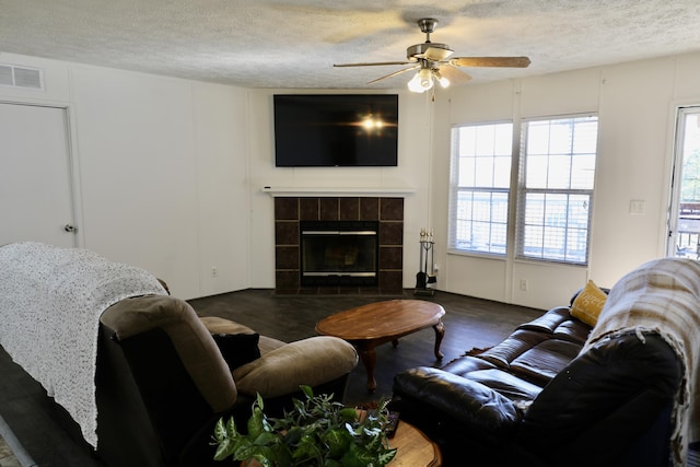 living room featuring a textured ceiling, dark hardwood / wood-style flooring, ceiling fan, and a tiled fireplace