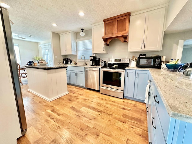 kitchen with a kitchen island, stainless steel appliances, white cabinets, a textured ceiling, and light hardwood / wood-style floors