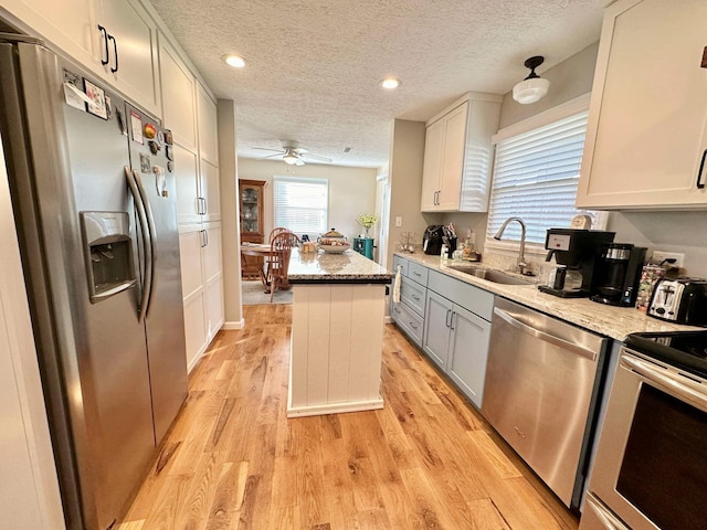 kitchen featuring light wood-type flooring, stainless steel appliances, a kitchen island, a sink, and ceiling fan