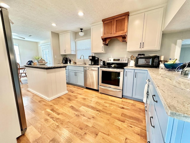 kitchen with a textured ceiling, light wood-style flooring, stainless steel appliances, recessed lighting, and light stone counters