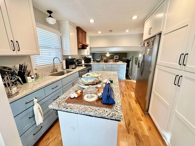 kitchen with a sink, a kitchen island, gray cabinetry, stainless steel appliances, and light wood-style floors