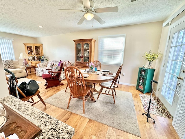 dining space with baseboards, a textured ceiling, light wood-style flooring, and a ceiling fan