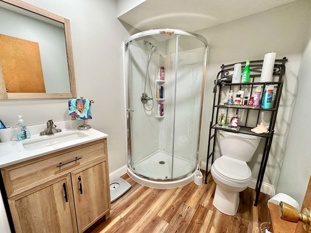 bathroom featuring vanity, toilet, baseboards, a stall shower, and wood finished floors