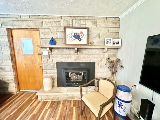 living area featuring crown molding, a stone fireplace, a textured ceiling, and hardwood / wood-style flooring