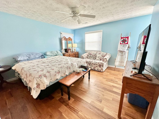 bedroom featuring light wood finished floors, a textured ceiling, baseboards, visible vents, and ceiling fan