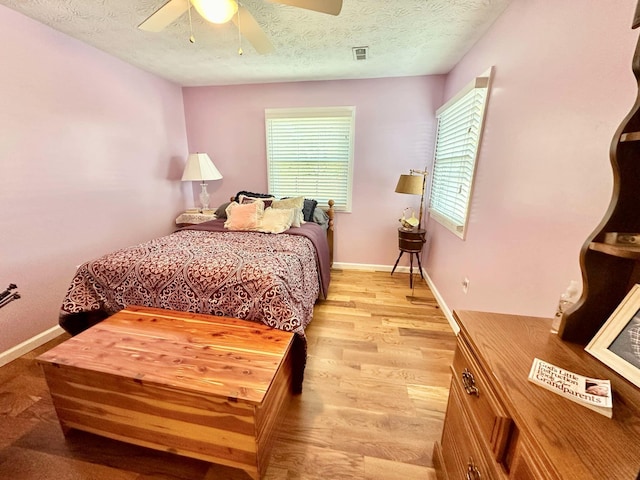 bedroom with a textured ceiling, multiple windows, light wood-type flooring, and ceiling fan