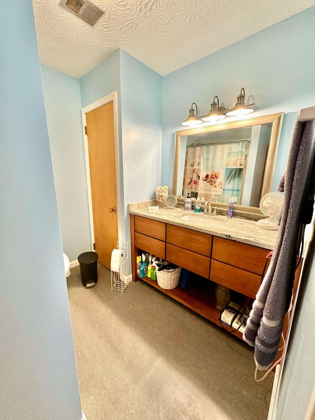 bathroom with vanity, a textured ceiling, baseboards, and visible vents
