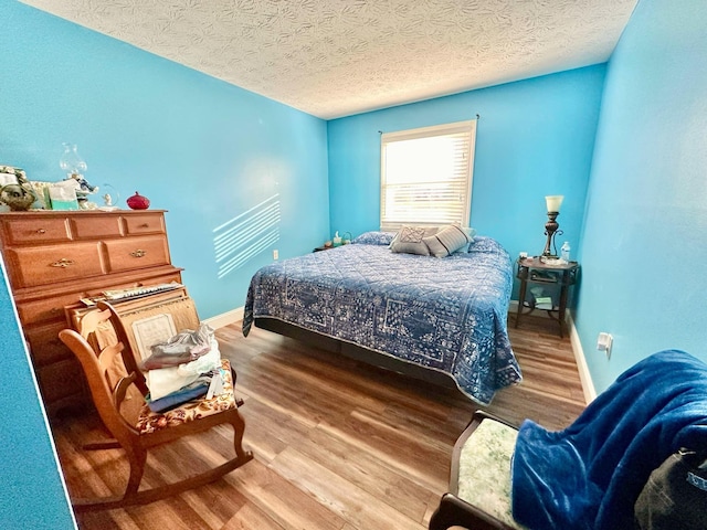 bedroom featuring baseboards, wood finished floors, and a textured ceiling