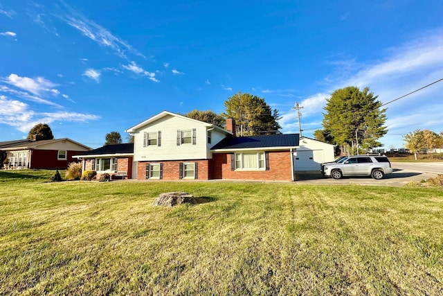 split level home featuring brick siding, a front yard, and a chimney