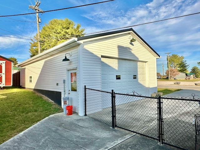 view of side of property featuring a gate, fence, a detached garage, a lawn, and an outbuilding