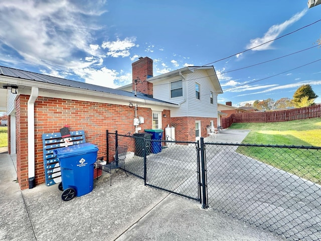 view of home's exterior with a gate, fence, a chimney, brick siding, and a yard