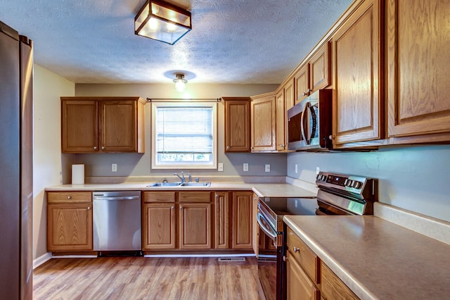 kitchen with light hardwood / wood-style flooring, a textured ceiling, appliances with stainless steel finishes, and sink