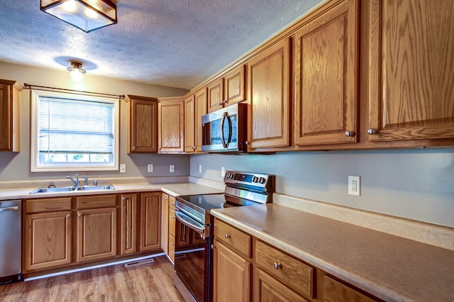 kitchen with stainless steel appliances, a textured ceiling, sink, and light wood-type flooring