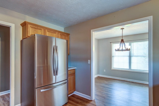 kitchen featuring hanging light fixtures, hardwood / wood-style floors, a chandelier, a textured ceiling, and stainless steel refrigerator