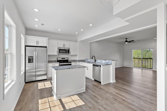 kitchen featuring appliances with stainless steel finishes, a center island, kitchen peninsula, white cabinets, and light hardwood / wood-style flooring