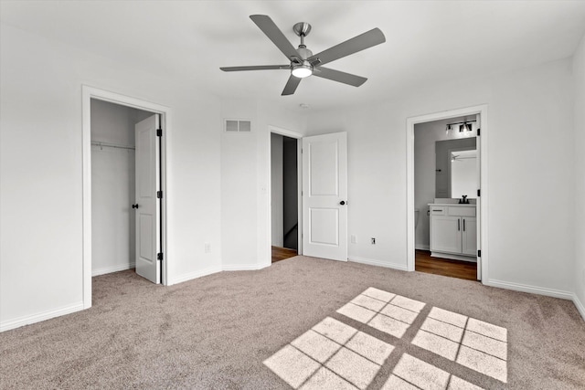 unfurnished bedroom with a closet, ensuite bath, carpet flooring, and ceiling fan