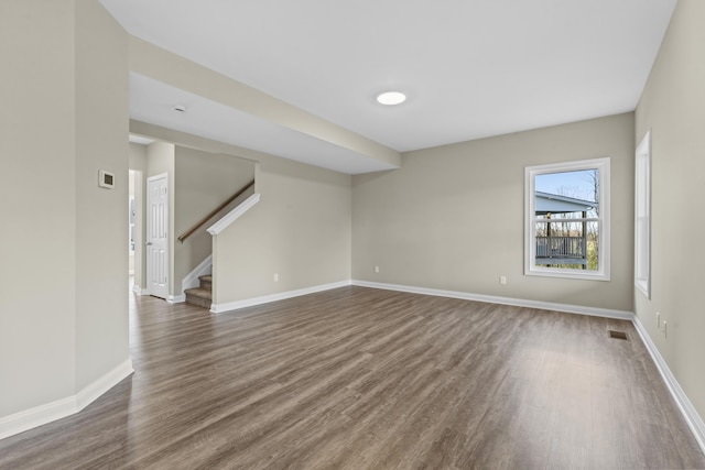 unfurnished room with dark wood-style floors, visible vents, stairs, and baseboards