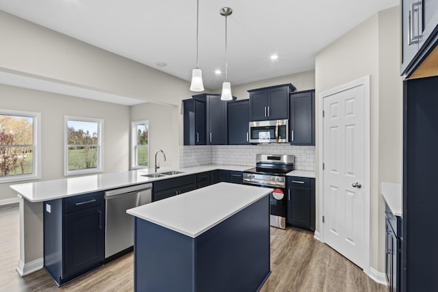 kitchen featuring a peninsula, a sink, light countertops, appliances with stainless steel finishes, and light wood-type flooring