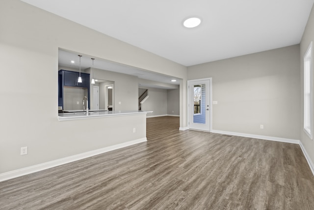 unfurnished living room with baseboards, dark wood finished floors, stairway, a sink, and recessed lighting