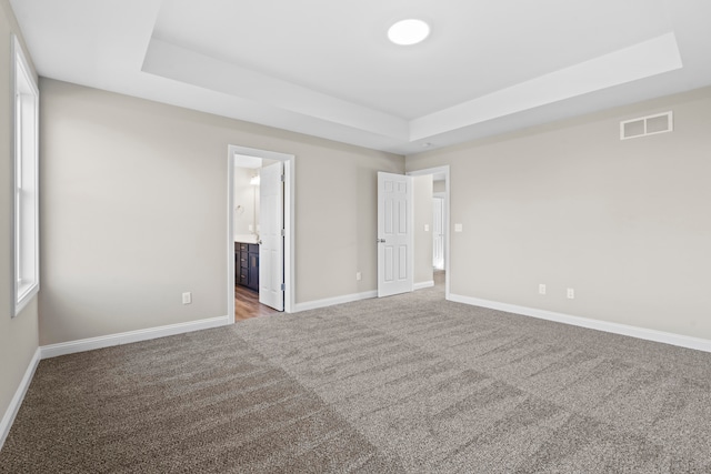 unfurnished bedroom featuring carpet flooring, a raised ceiling, and connected bathroom