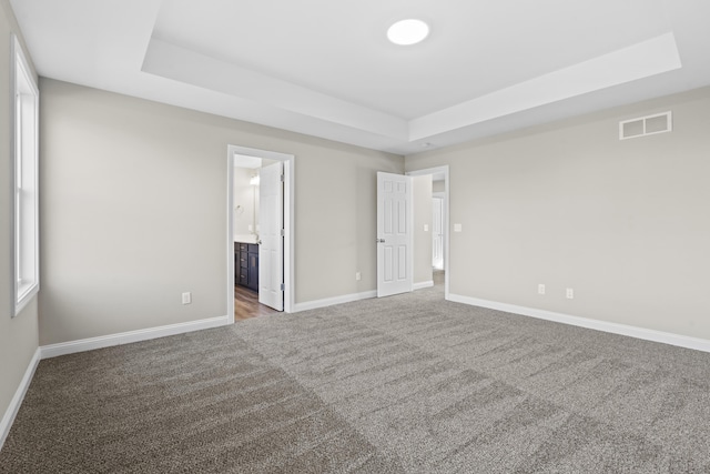 unfurnished bedroom with baseboards, visible vents, connected bathroom, a tray ceiling, and carpet flooring