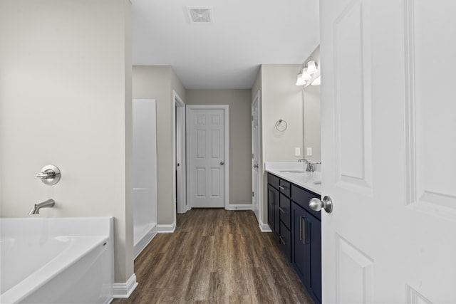 bathroom with visible vents, vanity, wood finished floors, baseboards, and a bath