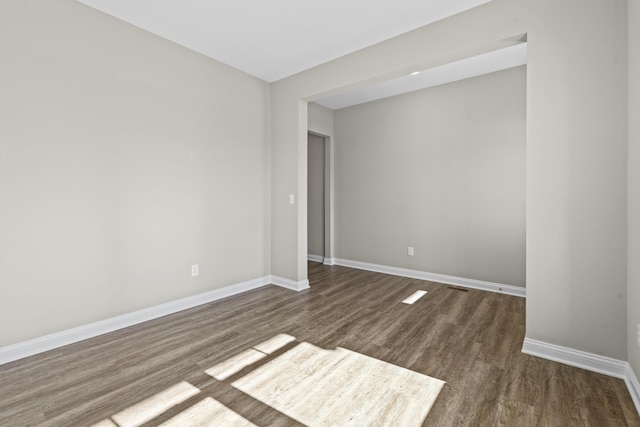 spare room with baseboards and dark wood-type flooring