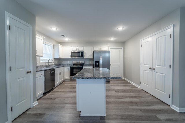 kitchen with white cabinets, a kitchen island, dark stone counters, light hardwood / wood-style flooring, and stainless steel appliances