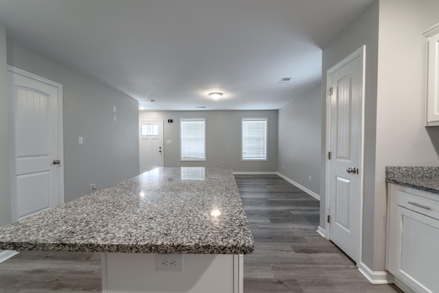 kitchen with white cabinets, light stone countertops, a center island, and dark hardwood / wood-style flooring