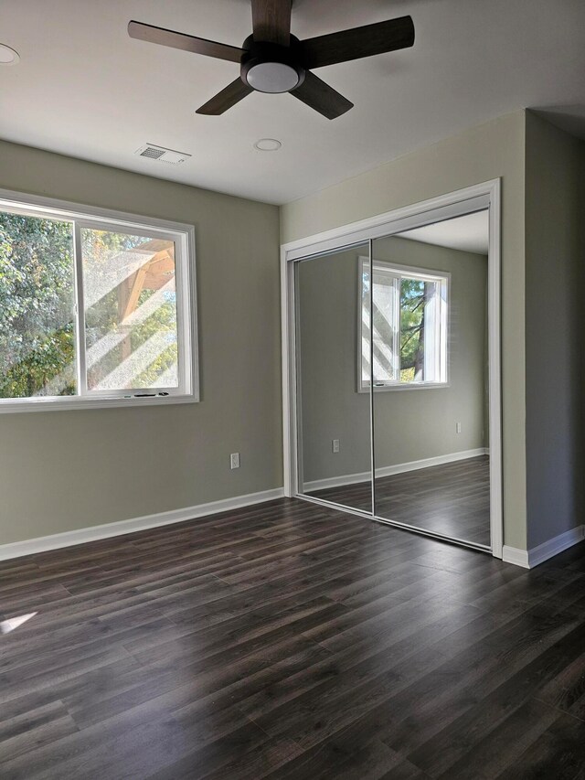 unfurnished bedroom featuring ceiling fan, multiple windows, and dark hardwood / wood-style floors