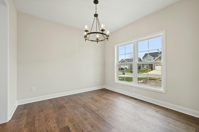 empty room with a chandelier, dark wood-style flooring, visible vents, and baseboards