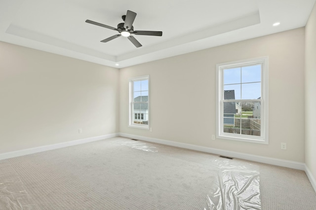 spare room with a tray ceiling, light colored carpet, visible vents, and baseboards