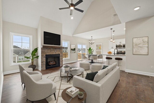 unfurnished living room featuring ceiling fan with notable chandelier, high vaulted ceiling, dark wood-type flooring, and a stone fireplace