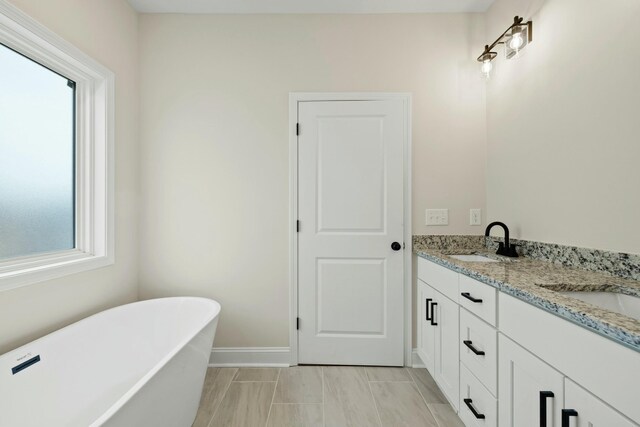 bathroom with double vanity, a freestanding tub, baseboards, and a sink