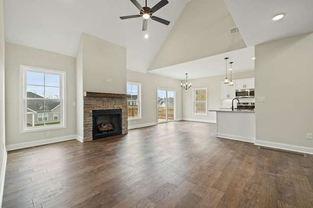 unfurnished living room featuring high vaulted ceiling, ceiling fan with notable chandelier, dark wood-style flooring, visible vents, and baseboards