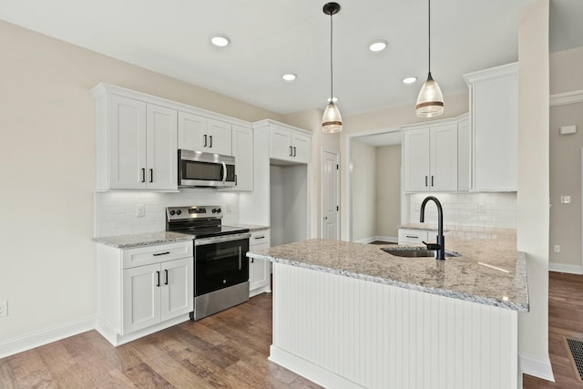 kitchen with white cabinets, appliances with stainless steel finishes, wood finished floors, a peninsula, and a sink