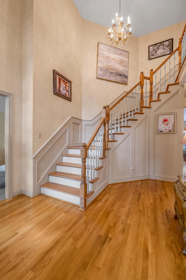 stairs featuring a notable chandelier, wood-type flooring, and a towering ceiling